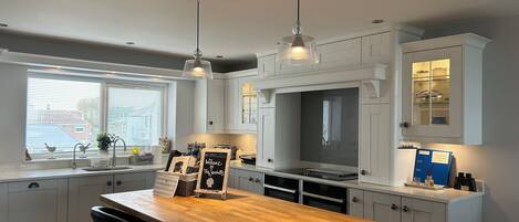 A modern kitchen with white cabinetry, a wooden island with bar stools, pendant lighting, and a view of the outside through a window.