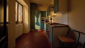 Eine schmale Küche mit Fenster, einer Mikrowelle und einem Stuhl.