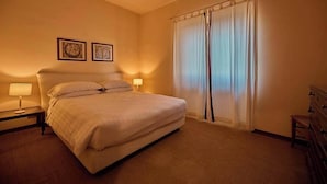 Ein ordentlich eingerichtetes Hotelzimmer mit einem großen Bett, zwei Nachttischlampen und einem Fenster mit transparenten Vorhängen.