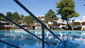 A clear swimming pool with a tiled deck, surrounded by trees and buildings. - Studio with shared pool-Beahost (Bibione)