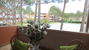 A balcony with wicker chairs, a glass vase with flowers, and a view of a building and trees. - Studio with shared pool-Beahost (Bibione)