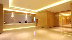 A hotel reception area with a wooden reception desk, two staff members, and a modern interior design.