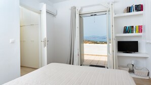 Une chambre à coucher comprenant un lit, une télévision, une bibliothèque et une porte donnant sur un balcon avec vue.