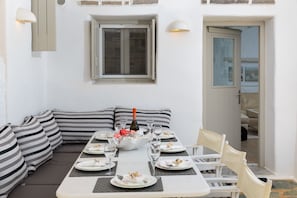 A dining area with a long table set for a meal, a sofa with striped cushions, and a window with a view.