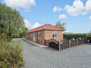 A small brick building with a red-tiled roof, a gravel driveway, and a wooden fence. - The New Build (Louth)