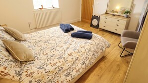 A bedroom with a bed, a dresser, a chair, a TV, and a window. - The New Build (Louth)