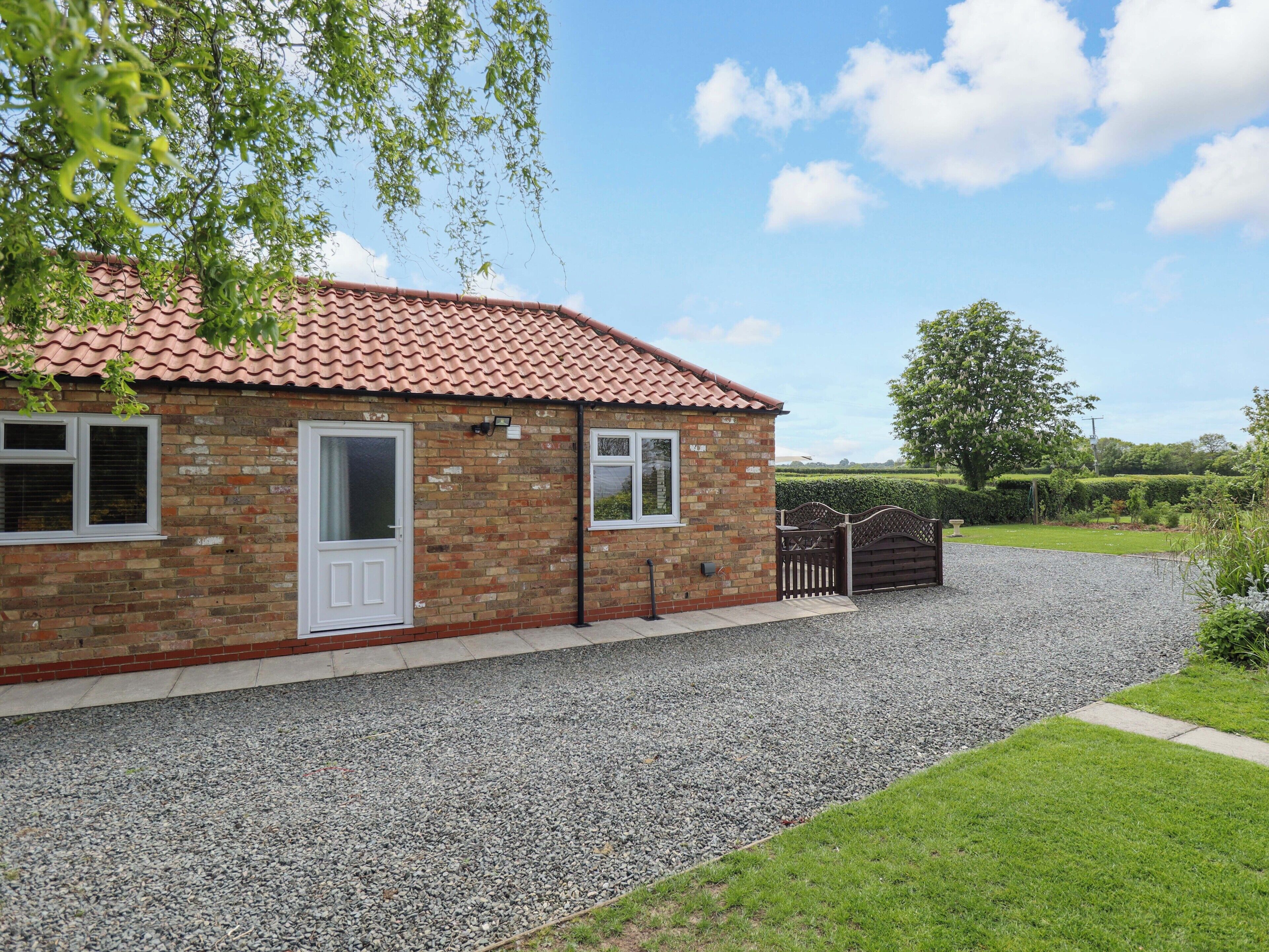 A brick house with a tiled roof, a gravel driveway, and a well-maintained lawn.
