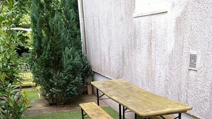 A patio with a wooden table and benches, surrounded by a well-maintained lawn and potted plants. - Lovely, very quiet vacation apartment for groups of up to 16 people (Bad Sachsa)