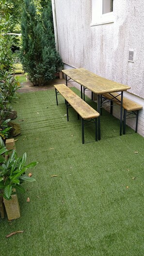 A patio with a wooden table and benches, surrounded by a well-maintained lawn and potted plants. - Lovely, very quiet vacation apartment for groups of up to 16 people (Bad Sachsa)