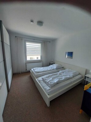 A small, single-room hotel bedroom with two beds, a window with blinds, a radiator, and a small bedside table. - Charming, very quiet vacation apartment for groups of up to 16 people (Bad Sachsa)