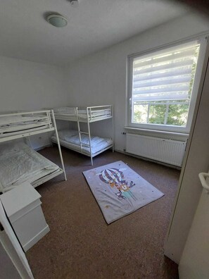 Une chambre d’enfant avec des lits superposés, un radiateur et une fenêtre avec des stores.