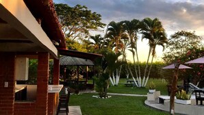 A patio area with a brick wall, a covered seating area, and a grassy lawn with palm trees.