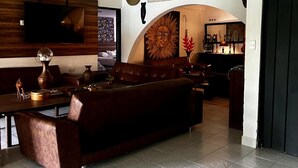 A modern living room with a large brown sofa, a flat-screen TV mounted on a wooden wall, and a decorative sun mural.