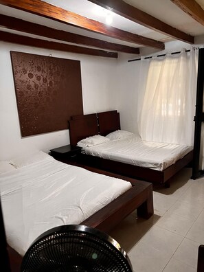 A room with two wooden beds, a large window with a floral design, and a ceiling fan.