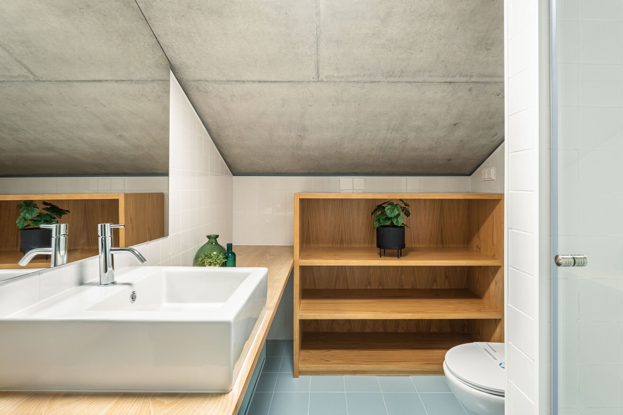 A modern bathroom with a large white sink, a wooden vanity, a toilet, and a concrete ceiling.