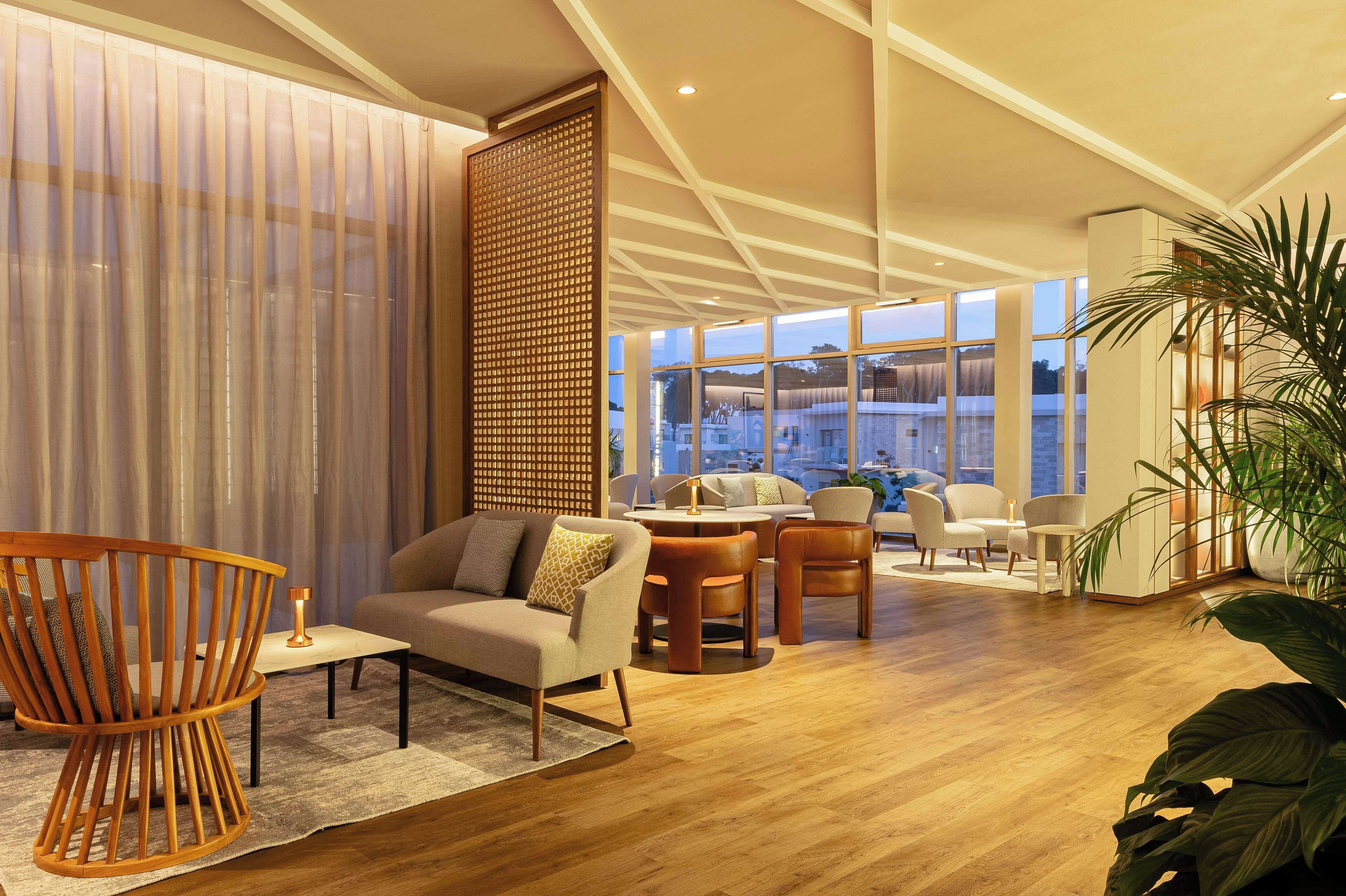 A modern living room with a sofa, chairs, a coffee table, and a large window offering a city view.