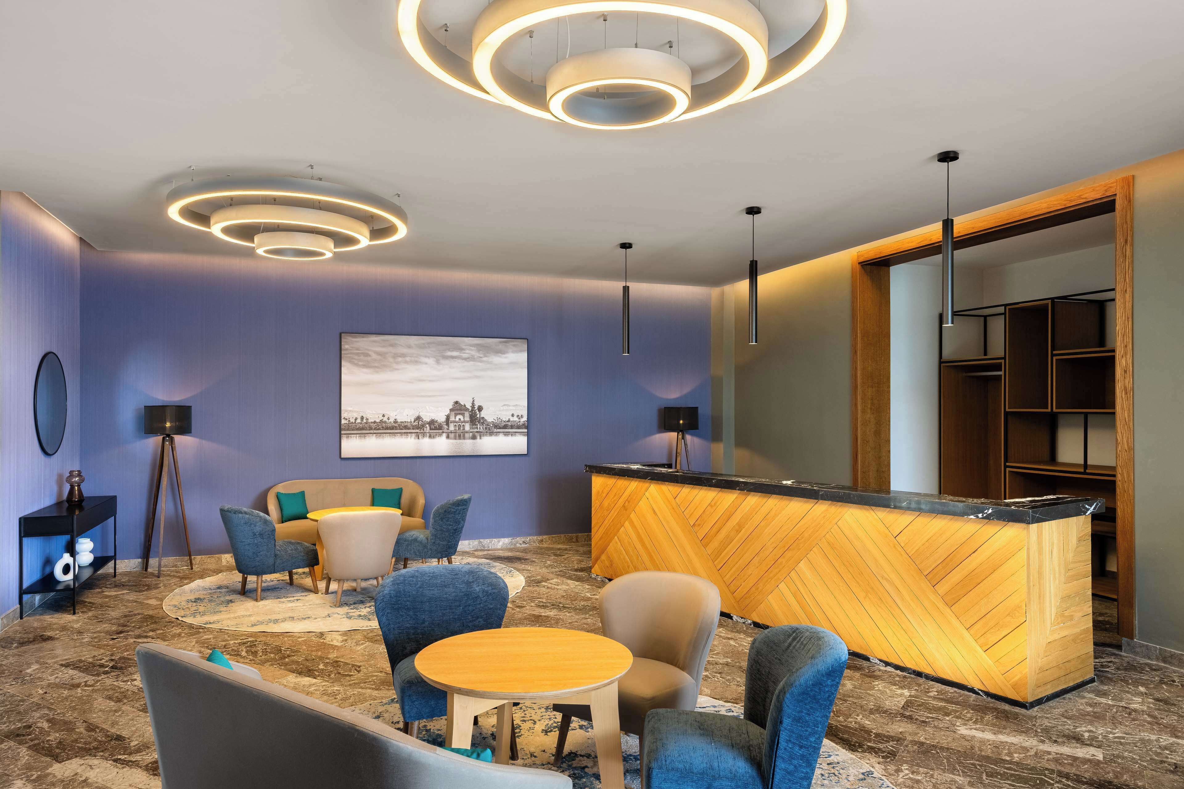 A modern hotel lobby with a reception desk, seating area, and a large wall-mounted artwork.