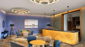 A modern hotel lobby with a reception desk, seating area, and a large wall-mounted artwork.