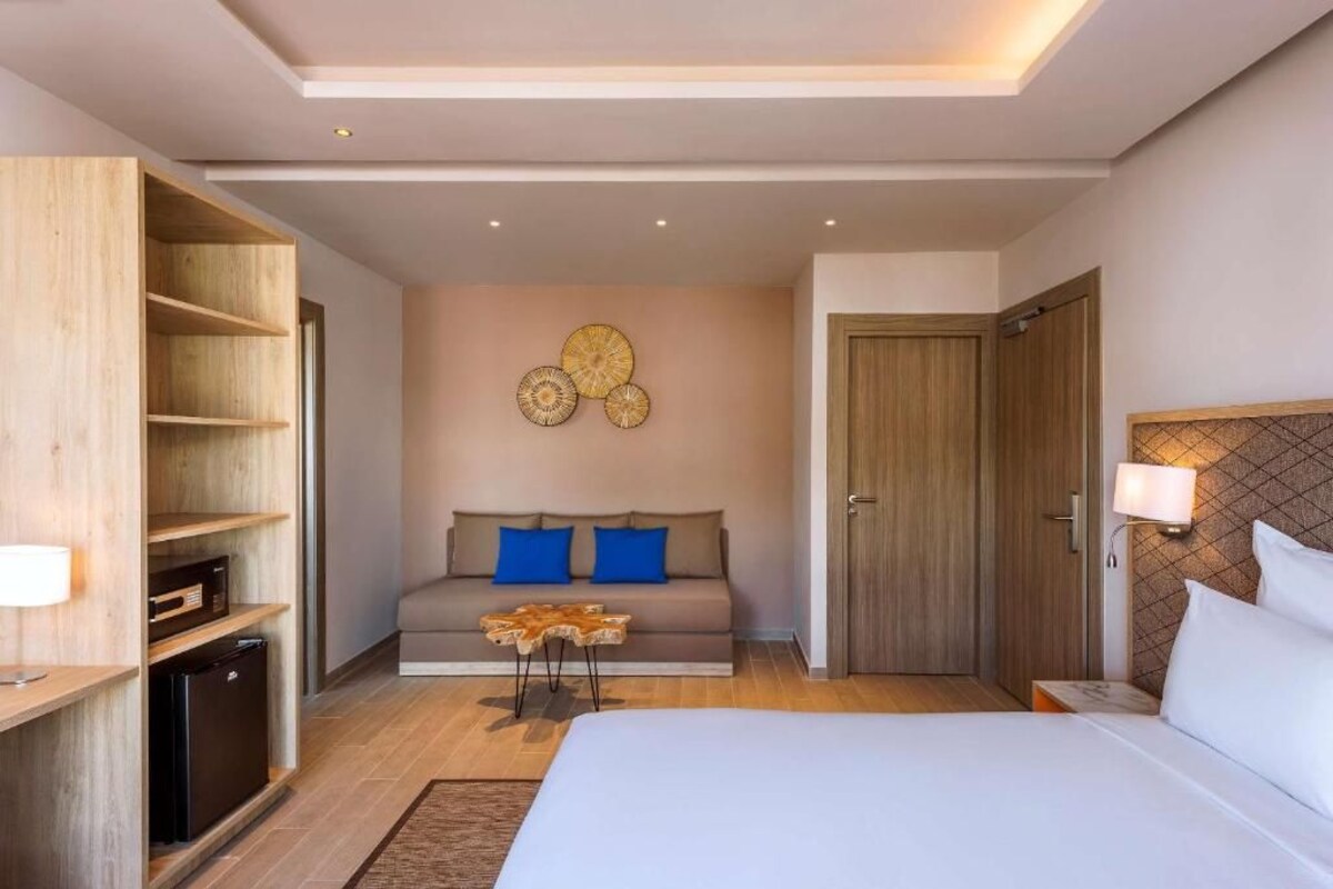 A modern hotel room with a bed, a sofa, a wooden wardrobe, and a wall-mounted lamp.