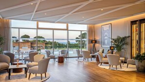 A spacious lounge area with multiple seating options, large windows offering a view of the city and a bridge, and a modern ceiling design. - Radisson Blu Resort, Al Hoceima (Ait Youssef Ou Ali)