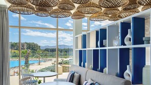 A modern room with a large window overlooking a pool and mountains, featuring a sofa, chairs, and decorative shelves. - Radisson Blu Resort, Al Hoceima (Ait Youssef Ou Ali)