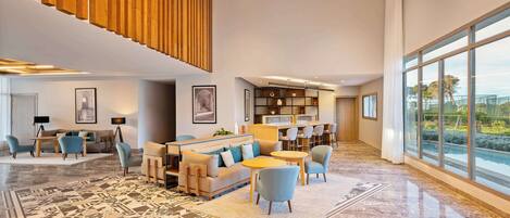 A spacious lobby with a high ceiling, a large window offering a view of the outdoors, a seating area with sofas and chairs, and a patterned floor.