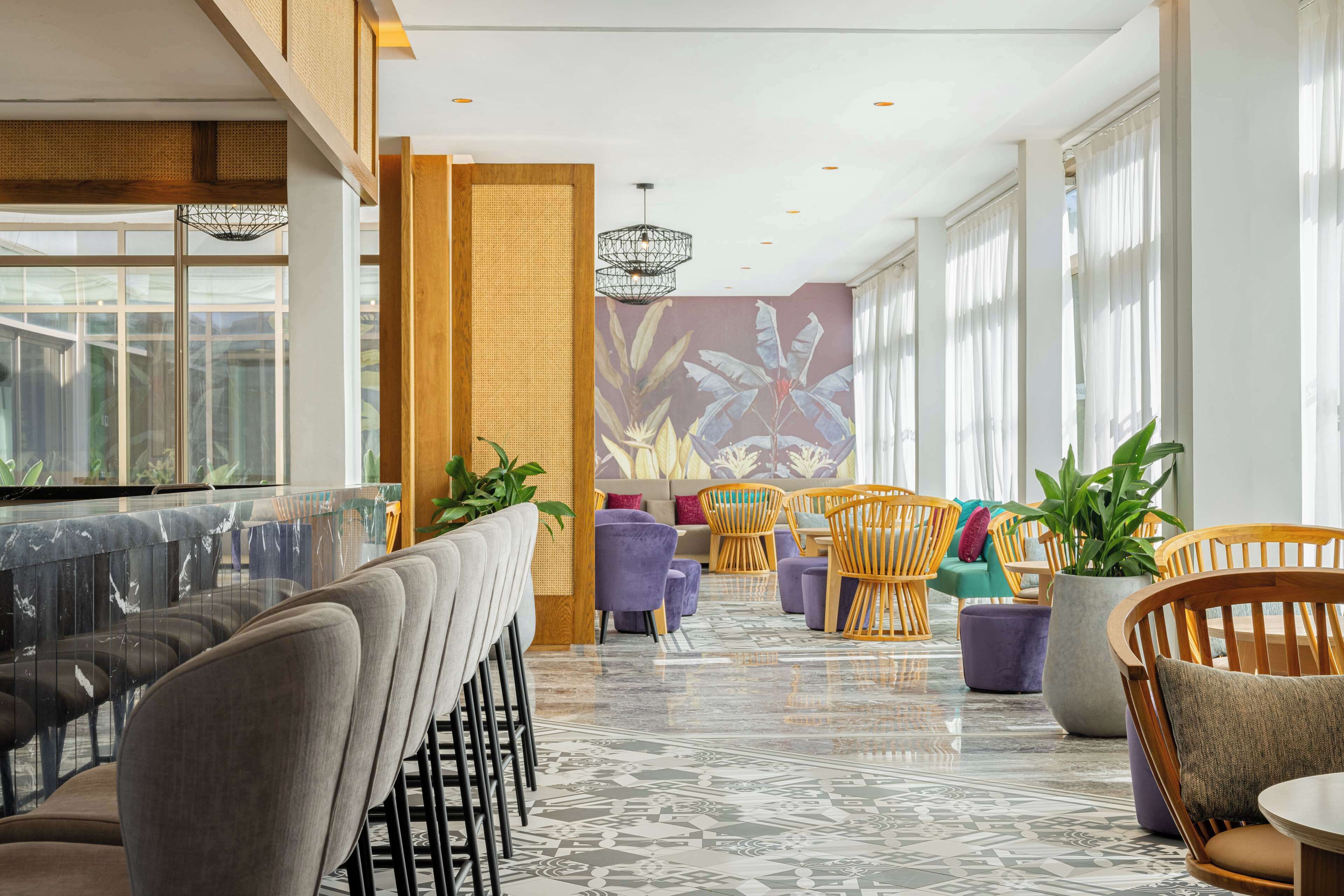 A modern interior with a bar area, seating with cushions, and a large window providing natural light.