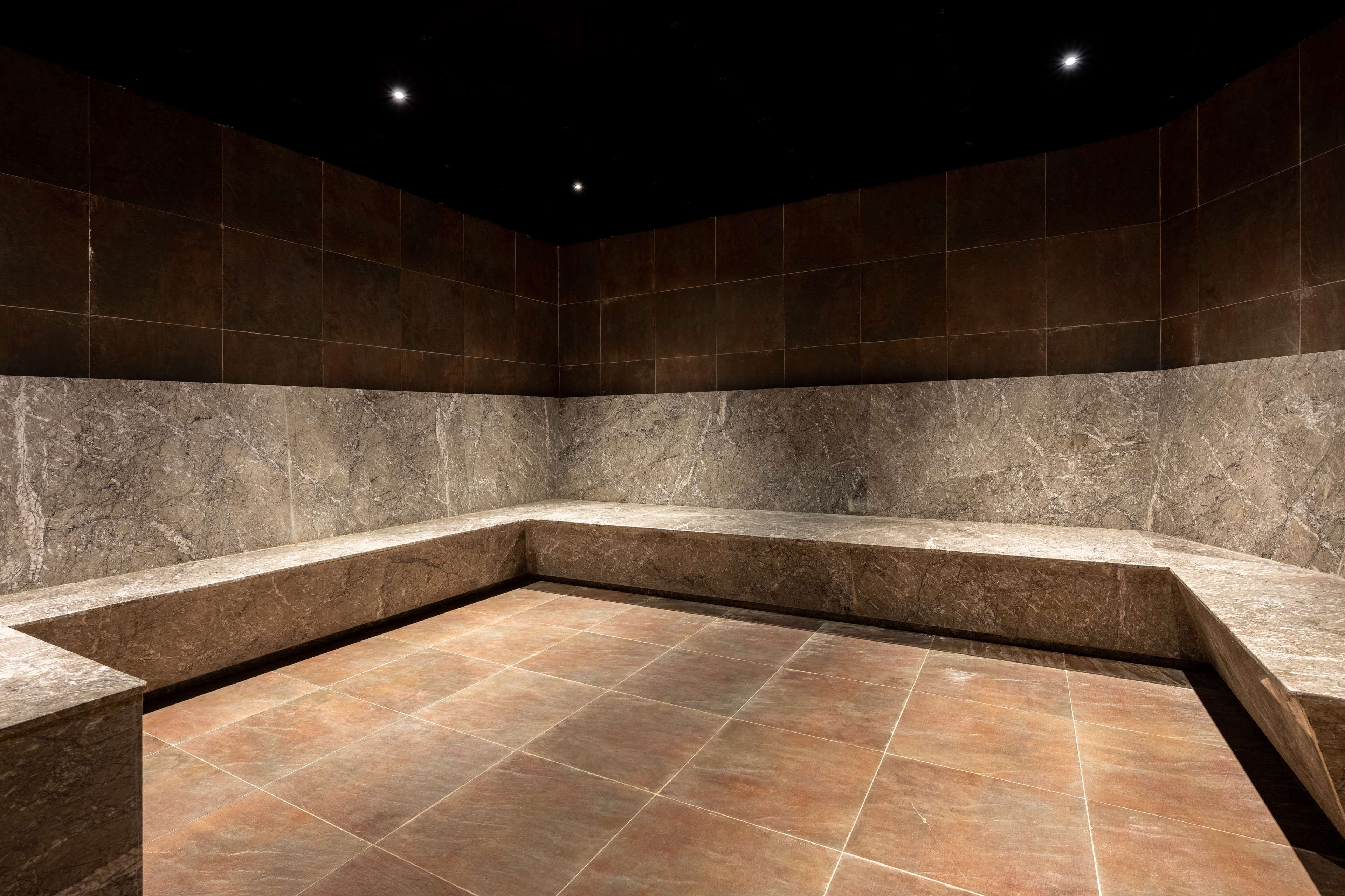 A modern bathroom with a marble floor and walls, featuring a corner sink and recessed lighting.