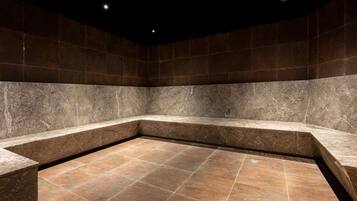A modern bathroom with a marble floor and walls, featuring a corner sink and recessed lighting.