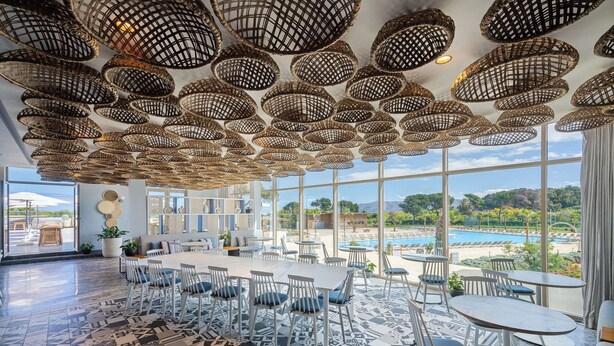 A spacious dining area with a large table and chairs, a patterned floor, and a view of a pool and mountains through large windows. - Radisson Blu Resort, Al Hoceima (Ait Youssef Ou Ali)