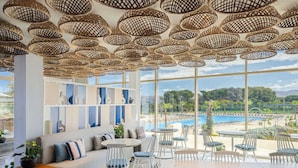 A modern lounge area with wicker ceiling lamps, a sofa, and chairs, overlooking a pool and beach. - Radisson Blu Resort, Al Hoceima (Ait Youssef Ou Ali)