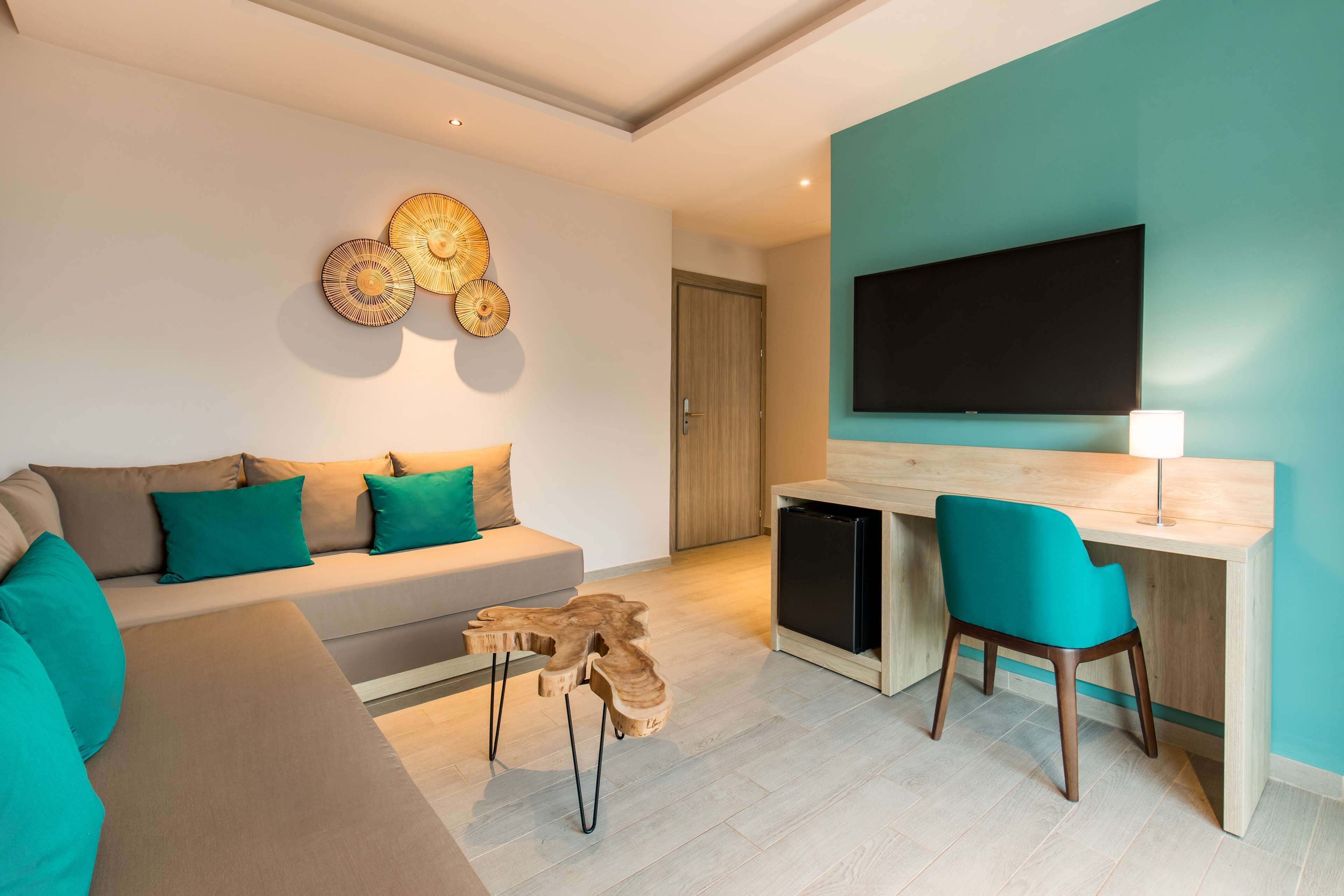 Una sala de estar moderna con un sofá, cojines color turquesa, una mesa de centro de madera y un televisor montado en una pared color turquesa.