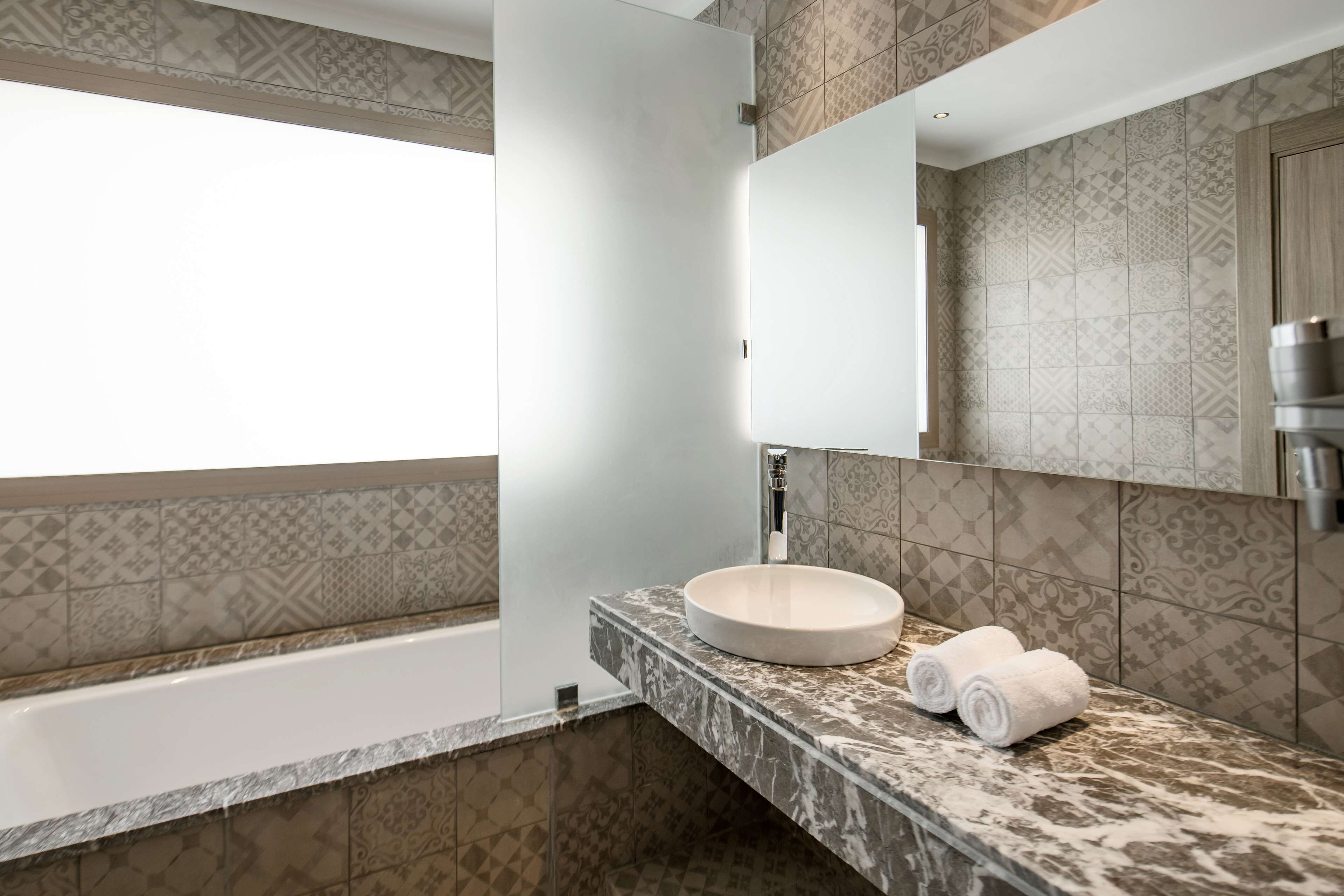 A modern bathroom with a bathtub, a round sink, and a large mirror.
