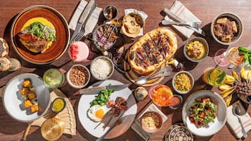 Diversos pratos, incluindo pizza, arroz, feijão e um ovo frito, sobre uma mesa de madeira.
