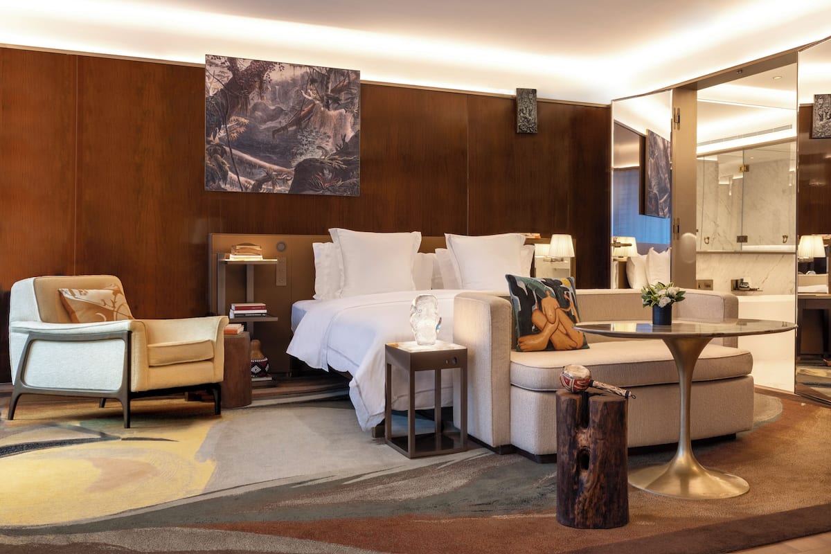 Ein modernes Hotelzimmer mit einem großen Bett, einer Sitzecke mit Sofa und Sesseln, einem kleinen Beistelltisch und einem runden Couchtisch.