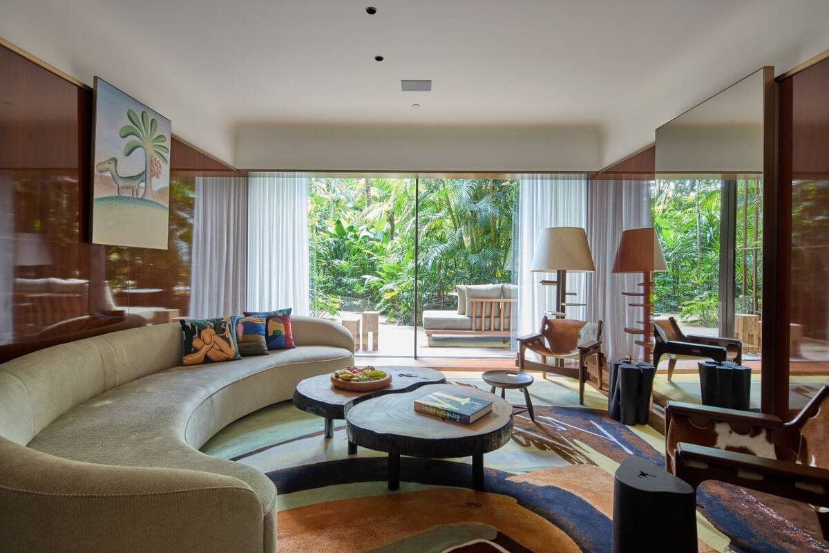 Ein modernes Wohnzimmer mit einer gebogenen Couch, einem Couchtisch und Blick auf üppiges Grün.