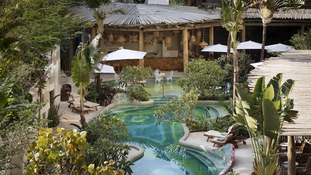 Ein Poolbereich mit Liegestühlen und Sonnenschirmen, umgeben von üppiger Bepflanzung und einer Holzpergola.