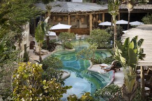 Un espace piscine agrémenté de chaises longues et de parasols, entouré d’une végétation luxuriante et d’une pergola en bois.