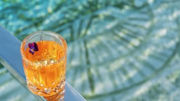 Een glas amberkleurige vloeistof met een paarse bloem op een reflecterend oppervlak.