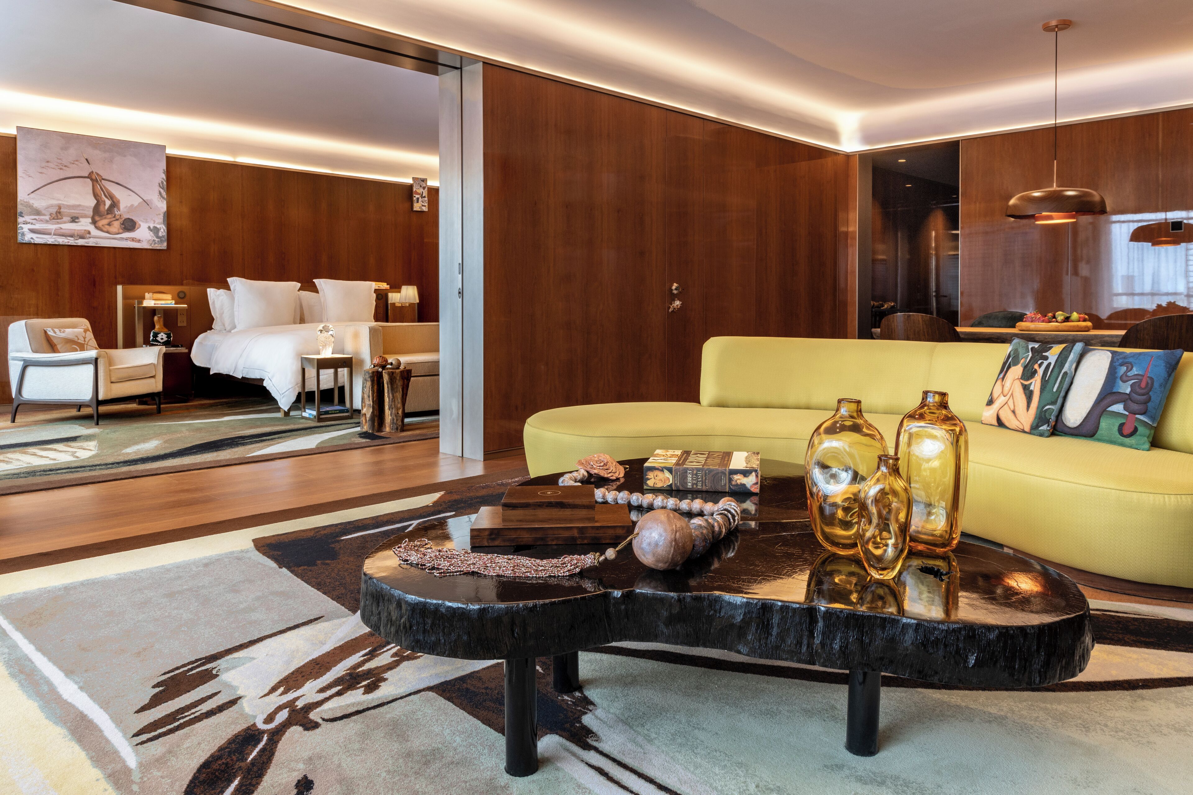A modern living room with a yellow sofa, a black coffee table with decorative items, and a wooden floor.