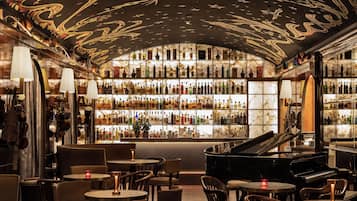Um bar com piano, mesas, cadeiras e uma estante cheia de garrafas de bebidas.