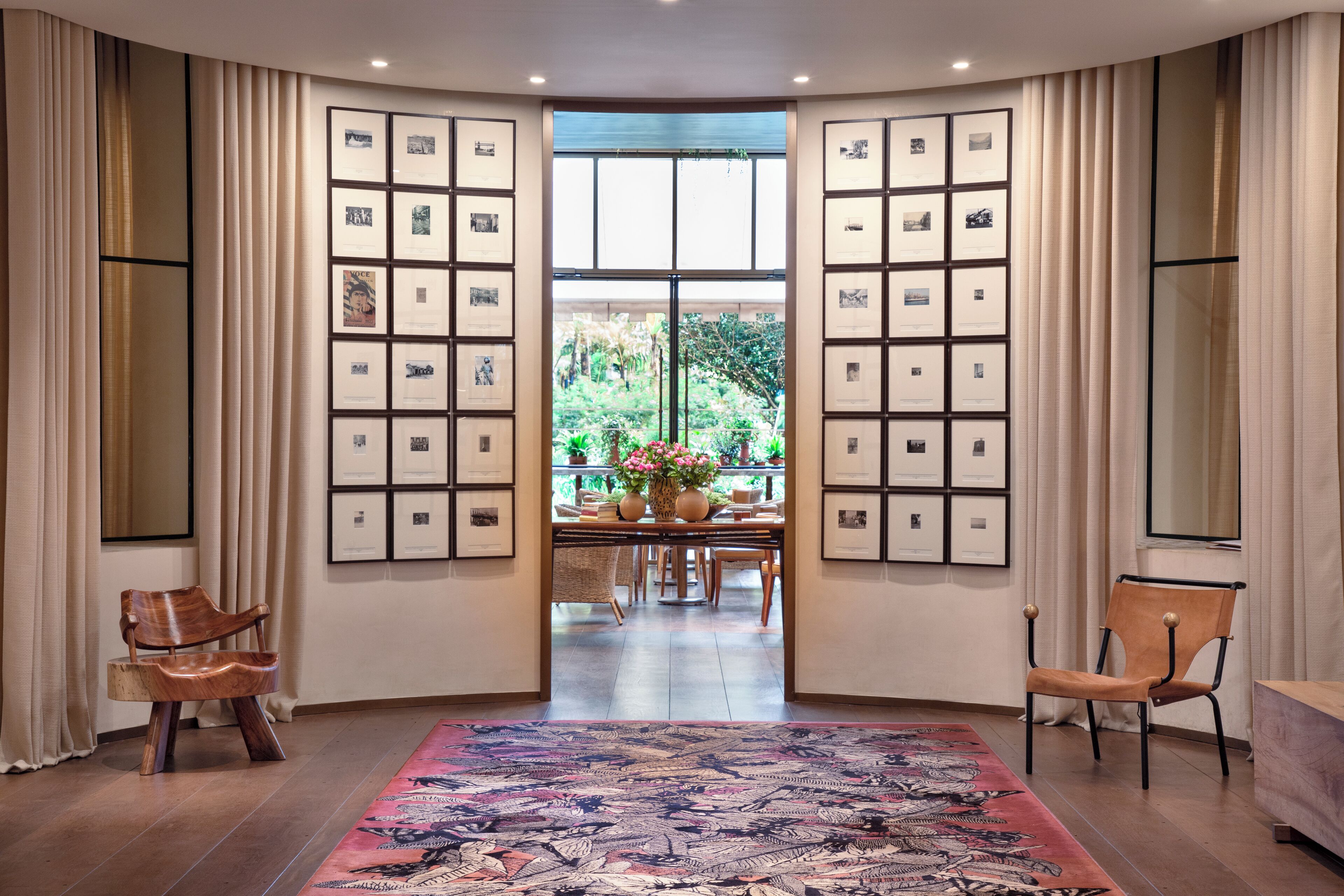A room with a large window, framed pictures on the walls, a patterned rug, and two wooden chairs.