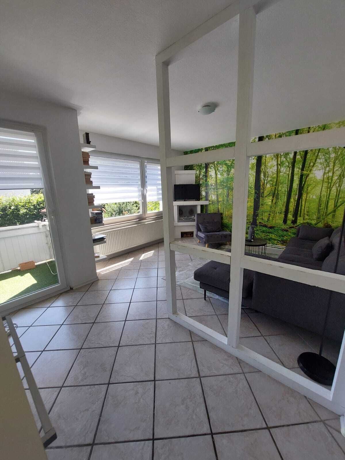A modern living room with a large window, a flat-screen TV, a grey sofa, and a white ceiling structure.