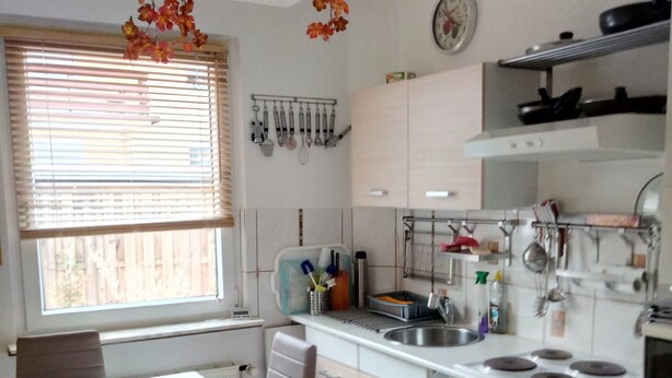 A kitchen with a dining table, chairs, a stove, and various kitchen utensils.
