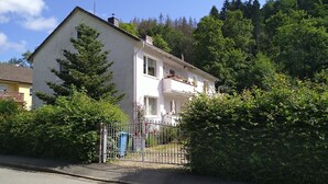 A two-story house with a balcony, surrounded by trees and a metal fence.