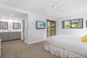 Une chambre à coucher avec un lit, un ventilateur de plafond, une télévision et une fenêtre donnant sur un jardin.