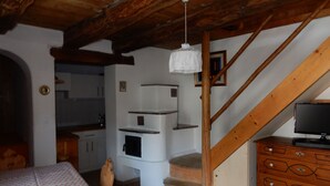 Ett rustikt rum med en trätrappa, en matplats med ett bord täckt av en mönstrad duk och en träbyrå med en tv.