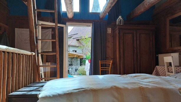 Ett rustikt rum med en säng av trä, en stege och utsikt över ett hus utanför.