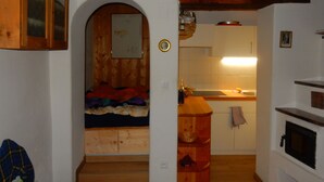 Ett mysigt kök med synliga träbjälkar, en inbyggd ugn och en liten matplats med en bänk.