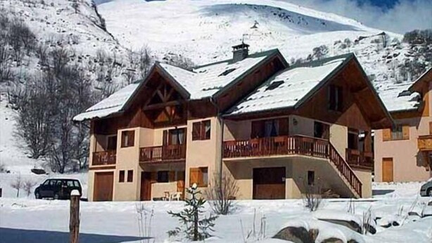 Un bâtiment de style chalet, avec une façade en bois et des balcons, entouré d’un paysage enneigé et de montagnes.